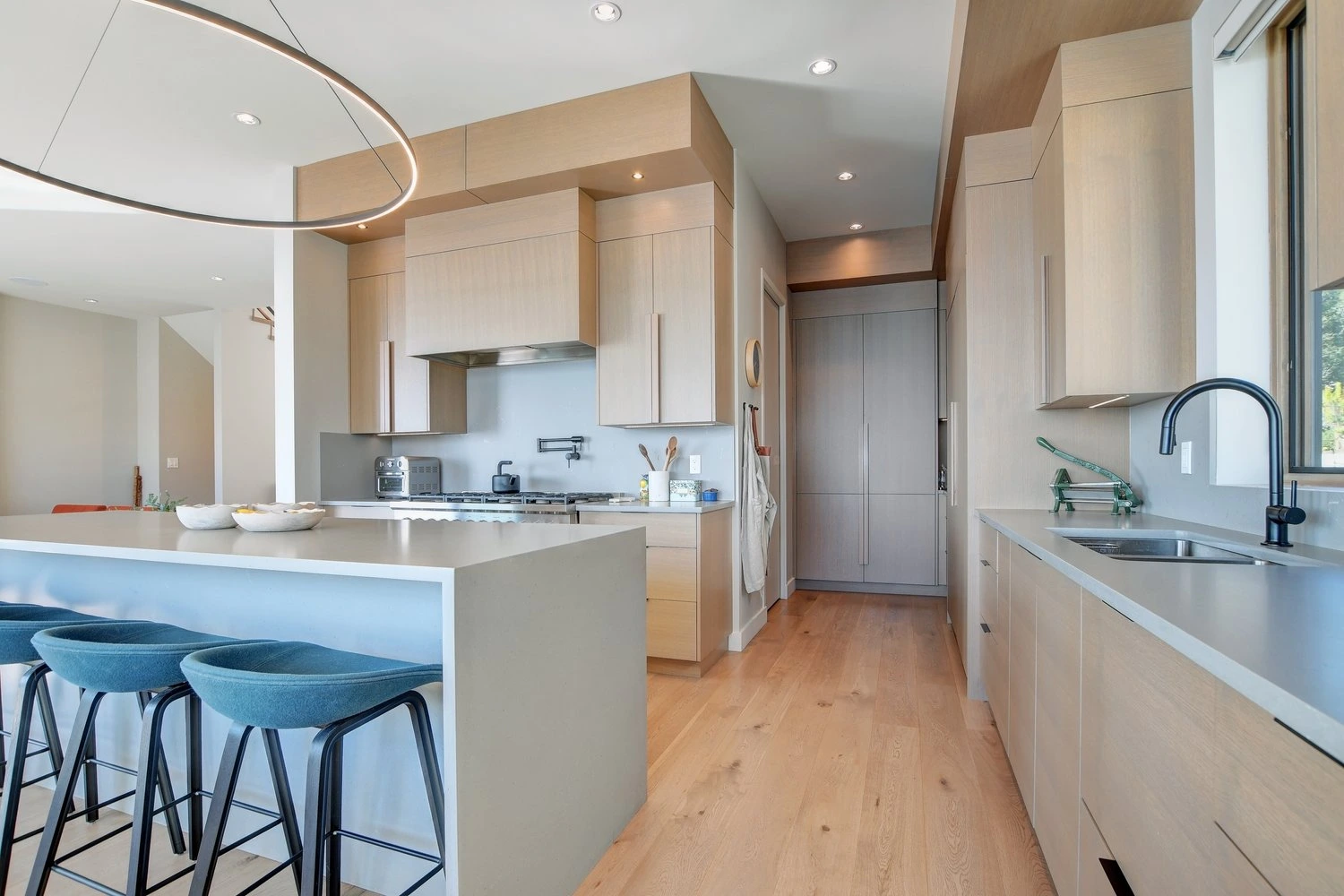 Modern kitchen with light wood cabinetry, curved architectural elements, and waterfront views
