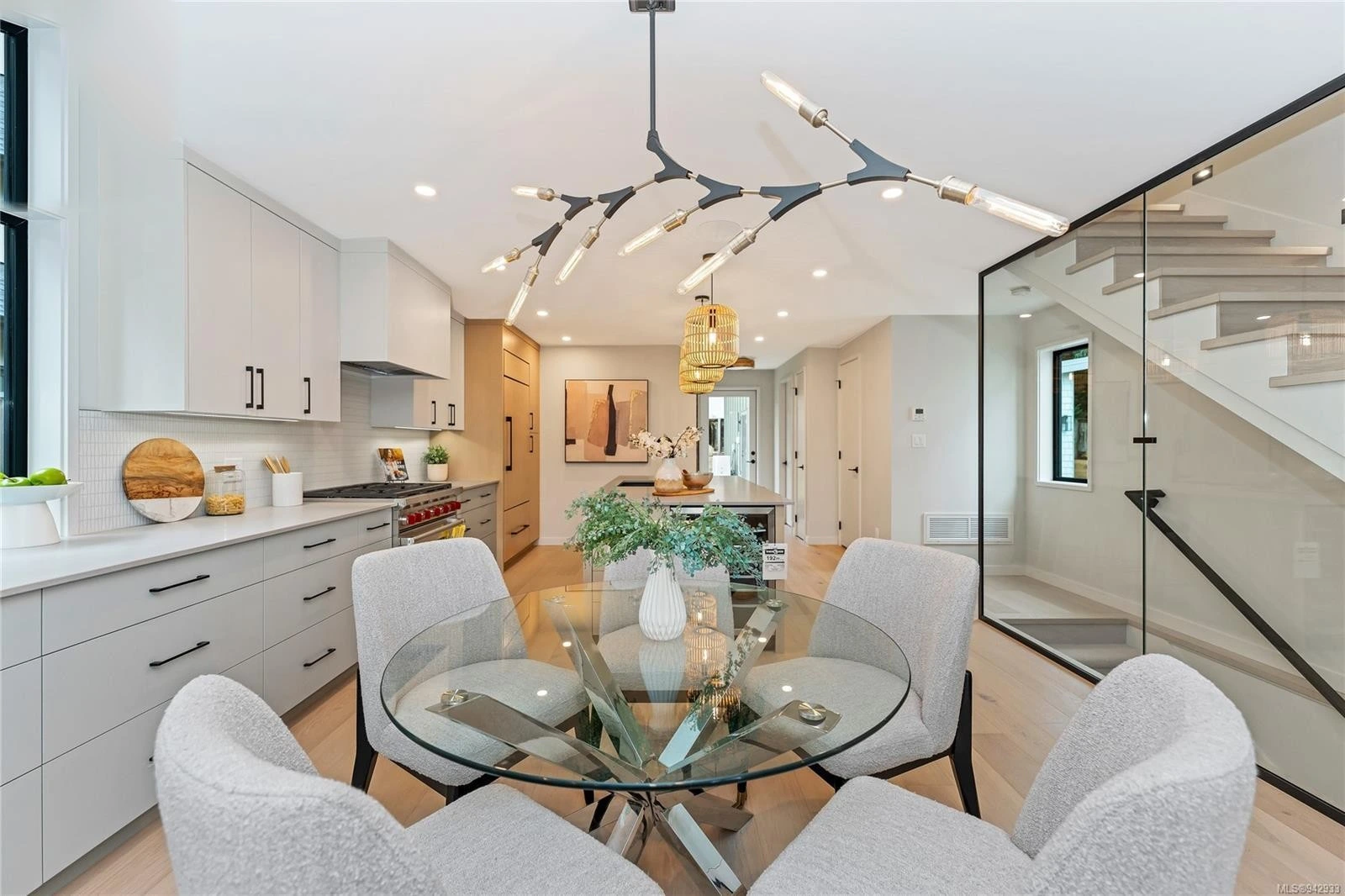 Spacious kitchen with white and wood cabinetry, featuring dining area with glass table and modern lighting